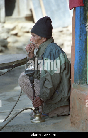 Vieux homme népalais fumeurs pipe de l'eau sur la rue Bahundanda village Zone de conservation de l'Annapurna au Népal Banque D'Images