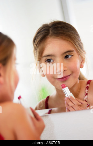 Jeune fille confiante avec de longs cheveux qui regarde sa réflexion sur un miroir comme elle joue et applique le maquillage. Banque D'Images