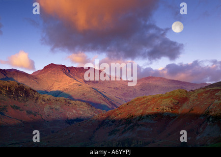 Les derniers rayons de soleil du soir faible lumière les fells que la pleine lune s'élève au-dessus des Langdale Pikes distinctif Banque D'Images
