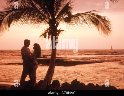 Couple sous palmier avec des boissons au coucher du soleil sur l'île de Maui Banque D'Images