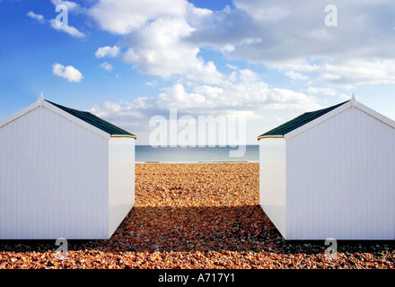 Cabines de plage blanc situé sur une plage de galets avec un ciel de nuages bas en toile de fond. Banque D'Images