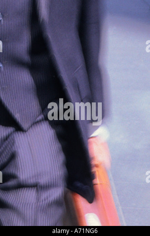 Gros plan de la section médiane d'un homme d'affaires bien habillé, dans un costume à épingles portant une mallette, marchant dans la rue. Banque D'Images