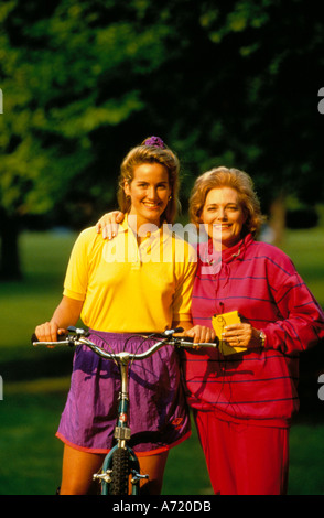 Portrait de plein air d'une mère portant des Walkman avec son bras autour des épaules de sa fille adulte qui est assis sur un vélo Banque D'Images