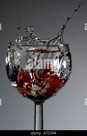 Red dice les projections dans un verre de vin rempli de liquide en action Banque D'Images