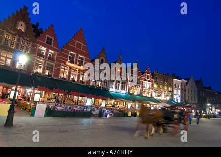 Vue de nuit horizontale grand angle d'une rangée de maisons traditionnelles à pignons dans la Markt (place du marché) avec un cheval et une calèche à Bruges. Banque D'Images