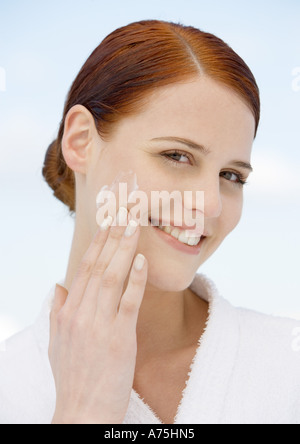 Woman applying moisturizer et wearing bathrobe Banque D'Images