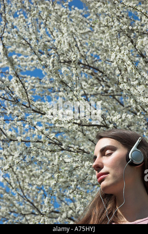 Jeune femme portant des écouteurs en arrière-plan des fleurs printemps Banque D'Images