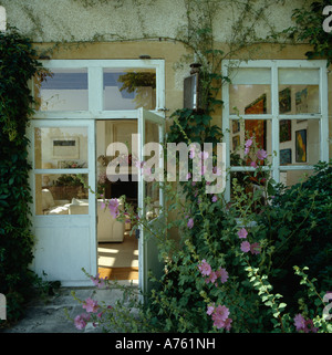 Lavatera rose en face de plus en plus maison en pierre avec double half-portes vitrées et vue de l'intérieur par la porte ouverte Banque D'Images