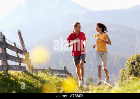 Jeune couple jogging par clôture en bois, montagnes en arrière-plans Banque D'Images