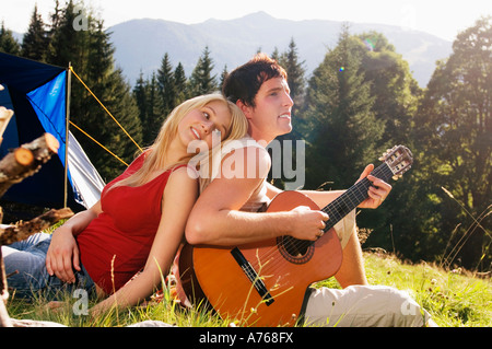 Young couple sitting in meadow, man playing guitar Banque D'Images