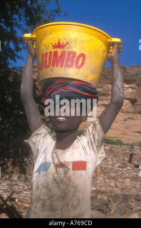 Un garçon Dogon transportant un gros seau d'eau sur sa tête, Tereli, Pays Dogon, au Mali. Banque D'Images