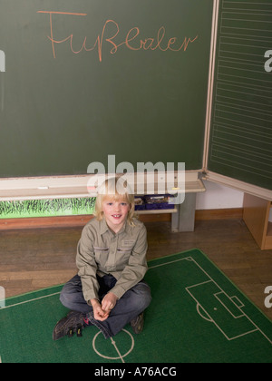 Boy sitting on floor in front of blackboard Banque D'Images