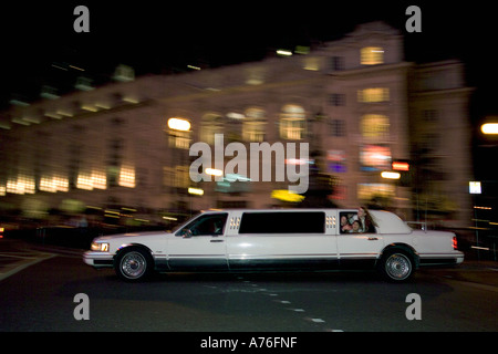 Une grande limousine blanche autour de Piccadilly Circus with motion blur en tenant les fêtards sur a night out. Banque D'Images