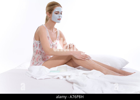 Femme avec masque de beauté sur le visage, sitting on bed Banque D'Images