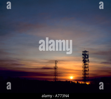 Coucher de soleil entre deux tours de communication, avec la pollution de l'air, à Buncefield North Downs, Kent, Angleterre, Royaume-Uni. Banque D'Images