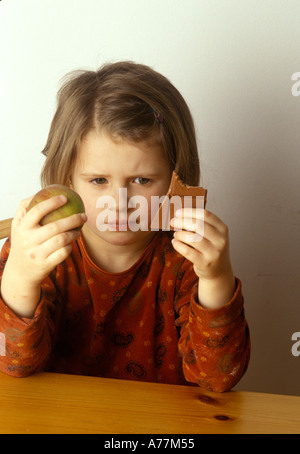 Girl Faire des choix entre une collation d'une pomme ou le chocolat malsain Banque D'Images