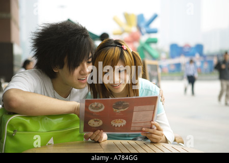 Teenage couple sitting at sidewalk cafe, à la recherche de menu à Banque D'Images