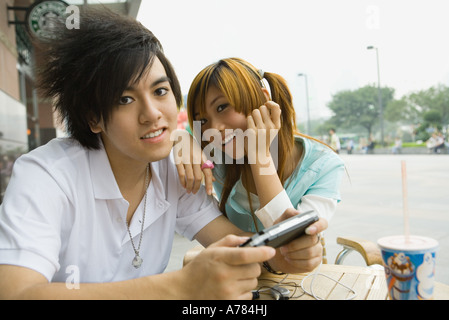 Teenage couple sitting at outdoor cafe, boy holding jeu vidéo Banque D'Images