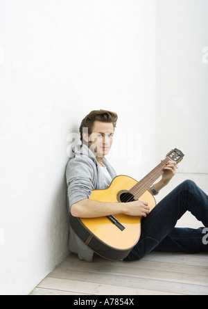 Jeune homme assis sur le sol, jouer de la guitare Banque D'Images