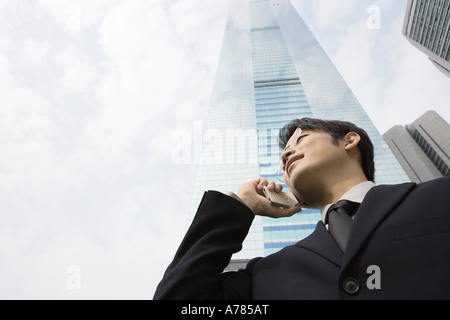 Young businessman using cell phone, gratte-ciel en arrière-plan, low angle view Banque D'Images