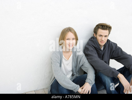 Jeune homme et femme assise sur le sol, leaning against wall Banque D'Images