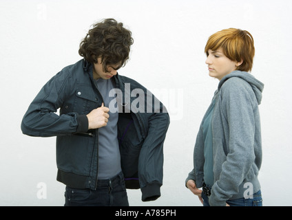 Jeune homme et femme debout, l'homme de mettre sur la veste tandis que Montres femme Banque D'Images