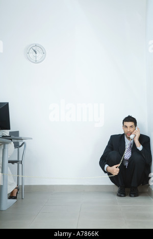 Businessman sitting on floor, en coin, parlant au téléphone Banque D'Images