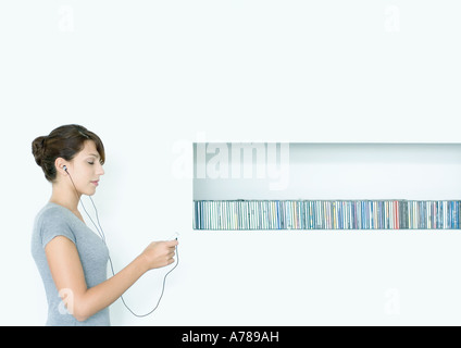 Jeune femme debout, listening to MP3 player, à côté de la rangée de CDs, les yeux fermés Banque D'Images