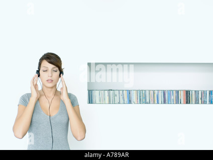 Jeune femme debout, l'écoute au casque, à côté de la rangée de CDs, les yeux fermés Banque D'Images