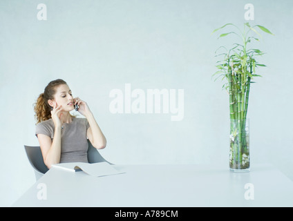Woman using cell phone, bloc de papier sur la table devant elle Banque D'Images