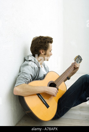 Jeune homme assis sur le sol, jouer de la guitare Banque D'Images