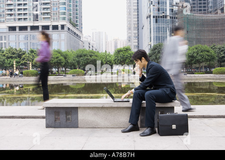 Businessman using laptop in office park, passants flous en arrière-plan Banque D'Images