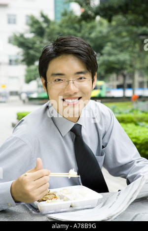 Businessman eating lunch avec des baguettes et de la lecture, cropped Banque D'Images