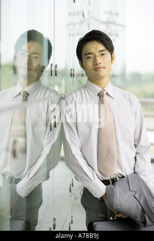 Businessman leaning against glass wall, portrait Banque D'Images