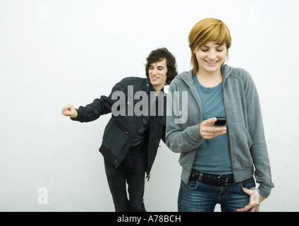 Young woman holding cell phone alors que jeune homme derrière elle des danses, fond blanc Banque D'Images