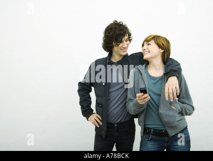 Jeunes adultes en couple, l'homme avec le bras autour de la femme, woman holding cell phone Banque D'Images