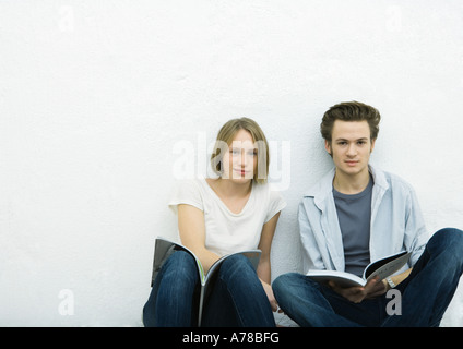 Adolescente et jeune homme assis sur le plancher avec des livres, looking at camera Banque D'Images