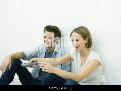 Adolescente et jeune homme assis sur le plancher, girl pointing remote control du bâti Banque D'Images