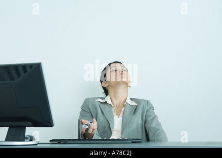 Businesswoman holding yinyang balls, sitting at desk, tête en arrière et les yeux fermés Banque D'Images