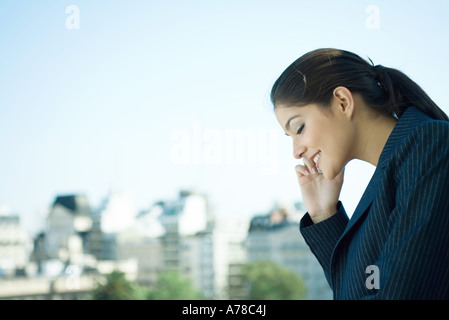 Businesswoman using cell phone, sur les toits de la ville en arrière-plan Banque D'Images