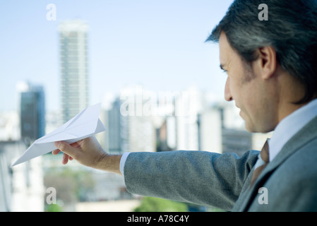 Businessman holding out paper airplane, skyline en arrière-plan Banque D'Images