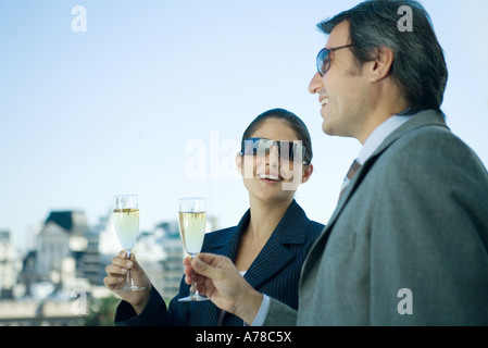 Partenaires d'affaires holding up verres de champagne, skyline en arrière-plan Banque D'Images