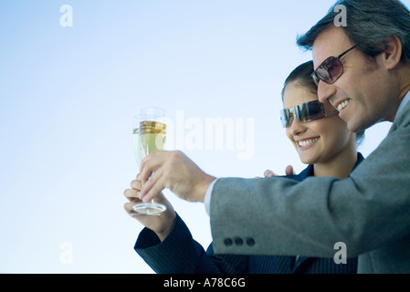 L'homme et la femme clinking glasses of champagne, ciel en arrière-plan Banque D'Images
