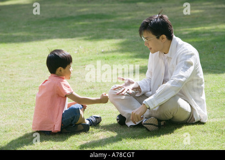 Père et fils assis sur l'herbe jouant "pierre papier ciseaux" Banque D'Images