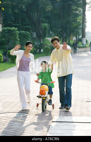 Boy riding bicycle, les parents des deux côtés, en agitant à huis clos Banque D'Images