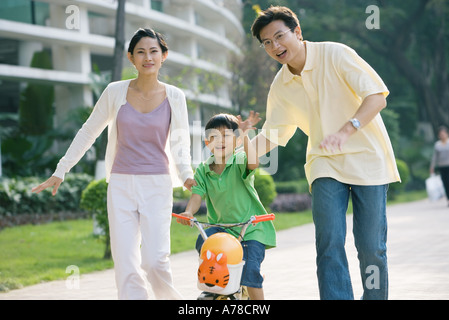 Boy riding bicycle, les parents des deux côtés, en agitant à huis clos Banque D'Images