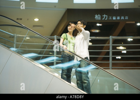 Dans l'escalator couple shopping mall, homme pointant hors du châssis Banque D'Images