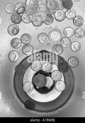 L'argent en bas du drain concept image avec des pièces de monnaie livre sterling autour d'évier en acier inoxydable bol de sortie des déchets Banque D'Images