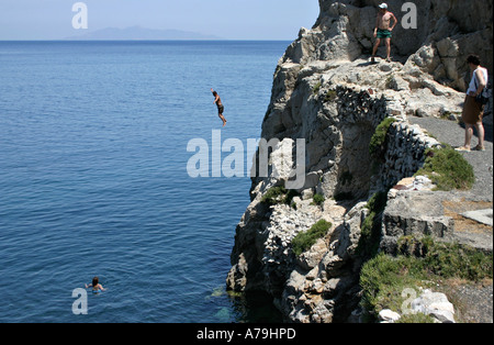 Saut rafraîchissant : un jeune homme saute de la falaise à la fin de la plage de Kamari dans l'eau bleu foncé a précédé une femme Banque D'Images