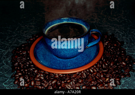 La cuisson à la vapeur du café noir dans une tasse bleue entourée de grains de café Banque D'Images
